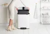 A woman is placing a dark gray bin into a white trash can in a kitchen. Náhľad obrázku produktu