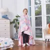 A young girl stands wrapped in a colorful unicorn-themed blanket in a room with a dresser, a plant, and a window. Náhľad obrázku produktu