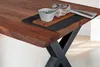 A close-up view of a wooden dining table with an X-shaped metal leg. Produktbild-Vorschau