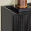 A close-up view of a black cabinet with fluted doors and a tray on top holding a decorative object and a lamp base. Náhľad obrázku produktu