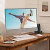 An all-in-one computer is set up on a wooden desk, displaying a video of a person dancing. A keyboard and mouse are in front of the computer, and other desk accessories are visible. Produktbild-Vorschau
