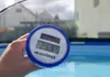 A hand holds a digital thermometer over a swimming pool. Anteprima dell’immagine prodotto