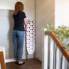 A woman is standing next to a polka-dot ironing board in a room with white doors and a wooden railing. Produktbild-Vorschau
