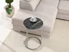 A round side table with a black marble top and silver legs is placed next to a light beige sectional sofa on a textured rug. A white teacup and saucer sit on the table. Náhled obrázku produktu