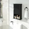 A black bathroom cabinet mounted on a white wall above a toilet, with a shower visible on the left. Podgląd zdjęcia produktu