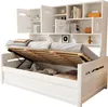 A white wooden bed frame with the mattress lifted, revealing storage space underneath. The bed has an integrated bookshelf unit above the headboard. Náhled obrázku produktu
