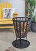 A fire pit with burning logs sits on a patio next to a yellow chair with an elephant pillow. Produktbild-Vorschau