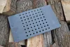 A rectangular cast iron grate with many circular holes lies on a pile of chopped firewood. Voir les images du produit