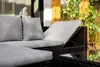 An outdoor lounge set with gray cushions on a brown rattan frame, placed on a patio with greenery and a wooden fence in the background. Náhled obrázku produktu