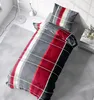 A bed with plaid bedding in a room with a lamp and a rug. Produktbild-Vorschau