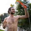 A man is showering outdoors with a portable camping shower near a body of water and trees. Voir les images du produit