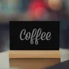 A small chalkboard sign with the word "Coffee" written on it, resting on a wooden stand. Anteprima dell’immagine prodotto