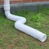 A white flexible drainpipe extension is connected to a downspout and laid out on the grass next to a brick wall. Produktbild-Vorschau