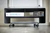 A black metal printer stand with wheels, holding a printer, a ream of paper, and two ink cartridges. Produktbild-Vorschau