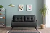 A dark gray sofa bed is shown in a living room setting with artwork on the wall and a plant in a basket. Náhled obrázku produktu