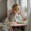 A baby is sitting in a high chair and eating. Voir les images du produit