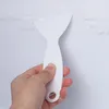A hand is holding a white plastic scraper, scraping frost off a white surface. Produktbild-Vorschau