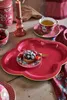 A table setting with a decorative plate, a tart, a cup of tea, and a candle. Produktbild-Vorschau