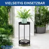 A black metal plant stand with two tiers, holding a potted plant on the top tier and books on the bottom tier, is placed in a bright, airy setting with lush green plants surrounding it. Podgląd zdjęcia produktu