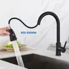 A black kitchen faucet with a pull-down sprayer is shown in use, with water spraying into a sink. A hand is holding the sprayer, and a digital display is visible on it. A bowl of grapes is also in the scene. Produktbild-Vorschau
