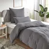 A bed with grey bedding, pillows, and a bedside table with a lamp and decorative items. Produktbild-Vorschau