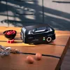 A black waffle maker sits on a wooden table, with a bowl of raspberries and two eggs nearby. Kitchen cabinets are visible in the blurred background. Produktbild-Vorschau