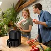 A couple is in a kitchen, looking at a tablet and preparing ingredients. An air fryer is on the counter. Anteprima dell’immagine prodotto