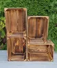 Four wooden crates are stacked in front of a green hedge. Náhled obrázku produktu