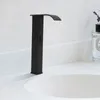 A black waterfall faucet is shown installed on a white countertop next to a sink. A bottle of perfume with lavender sprigs is visible in the background. Podgląd zdjęcia produktu
