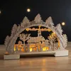 A wooden Christmas decoration with a village scene illuminated by warm white LEDs. Náhľad obrázku produktu
