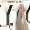 Several black coat hooks mounted on a white wall, with one hook displaying a beige jacket and another a rope. Produktbild-Vorschau