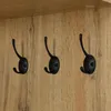 A close-up view of three black coat hooks mounted on a wooden panel. Produktbild-Vorschau