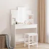 A white vanity table with a mirror and stool, decorated with perfume bottles and a plant, next to a window with beige curtains and a woven basket with a blanket. Produktbild-Vorschau
