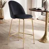 A black velvet bar stool with gold legs is placed next to a small round table in a well-lit room. Voir les images du produit