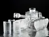 A glass decanter shaped like a tank, filled with a clear liquid, sits on a reflective surface next to three shot glasses. The background is black. Podgląd zdjęcia produktu
