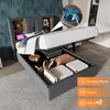 A bed with storage is shown with its storage compartment open, revealing various items inside. A close-up inset shows a phone charging wirelessly. Náhľad obrázku produktu