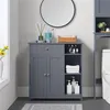 A grey bathroom cabinet with two doors and shelves is shown in a bathroom setting, with a toilet to the right and a vase with yellow flowers to the left. Produktbild-Vorschau