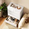 A white dresser with an open drawer filled with personal items, next to a plant and a sofa. Podgląd zdjęcia produktu