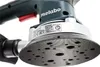 Close-up of a Metabo orbital sander, focusing on the sanding pad and a label with product information. Náhled obrázku produktu