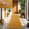 A hand touching a yellow rug in a hallway with plants and doors. Produktbild-Vorschau