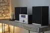 A micro stereo system with two speakers sits on a rustic wooden table. Voir les images du produit