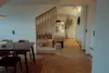 A dining table and chairs are in the foreground, with a wooden room divider separating it from a bedroom area with a massage table and a large potted plant. Produktbild-Vorschau