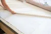 A person is putting a sheet on a bed, over a protective underpad. Podgląd zdjęcia produktu