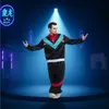 A man is posing in a retro tracksuit on a stage with spotlights and neon lights. Voir les images du produit