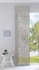 A panel curtain with a swirling pattern hangs in front of a window with a view of a tree and grass. A small white stool with a plant and a book sits to the left of the curtain.