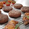 A close-up view of grilled food items, including burgers and chicken, arranged on a metal grill surface with some cherry tomatoes in the background. Produktbild-Vorschau