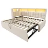A beige upholstered bed frame with a slatted mattress support system, shown in an open state to reveal its storage and pull-out components. The headboard features integrated LED lighting. Podgląd zdjęcia produktu