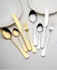 A collection of gold and silver cutlery arranged on a light gray surface, with two white plates in the background. Produktbild-Vorschau