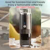 A portable coffee maker is shown on a table with a cup of coffee and some coffee beans, with a blurred background of a campsite and people enjoying themselves. Náhled obrázku produktu