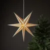 A paper star lantern hangs in front of a dark background and a Christmas tree. Podgląd zdjęcia produktu